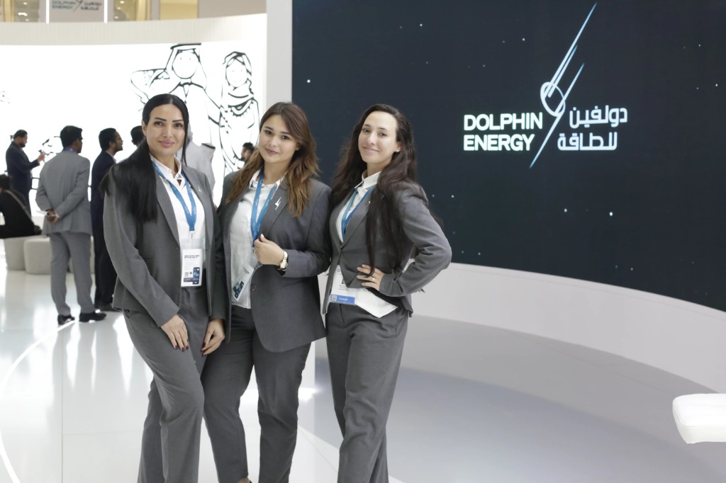Professional hostesses in grey blazers at an exhibitor booth during ADIPEC