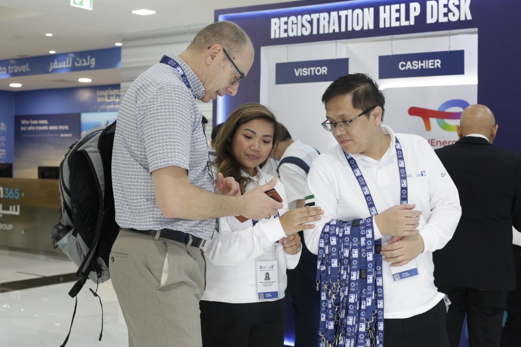 Registration help desk staff assisting a visitor at ADIPEC